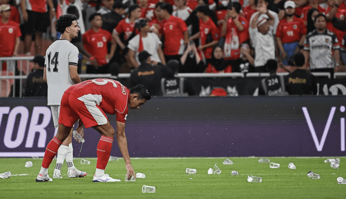 Trung vệ Indonesia Rizky Ridho (áo đỏ) dọn cốc nhựa do CĐV nhà ném xuống khi phản ứng trọng tài ở phút 77. Ảnh: Bola